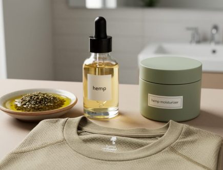 Glass hemp seed oil and skincare products on a vanity beside a folded neutral hemp-infused athleisure shirt, photographed in soft natural light.